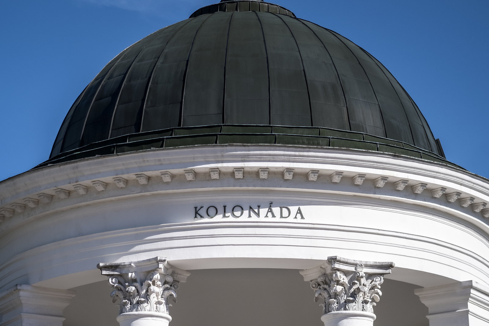 Detail of the dark dome and the Kolonáda lettering above a white cornice and Corinthian columns