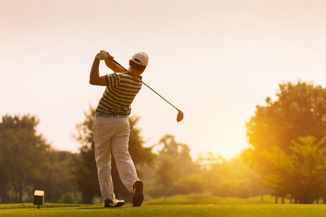 A golfer mid-swing at sunset