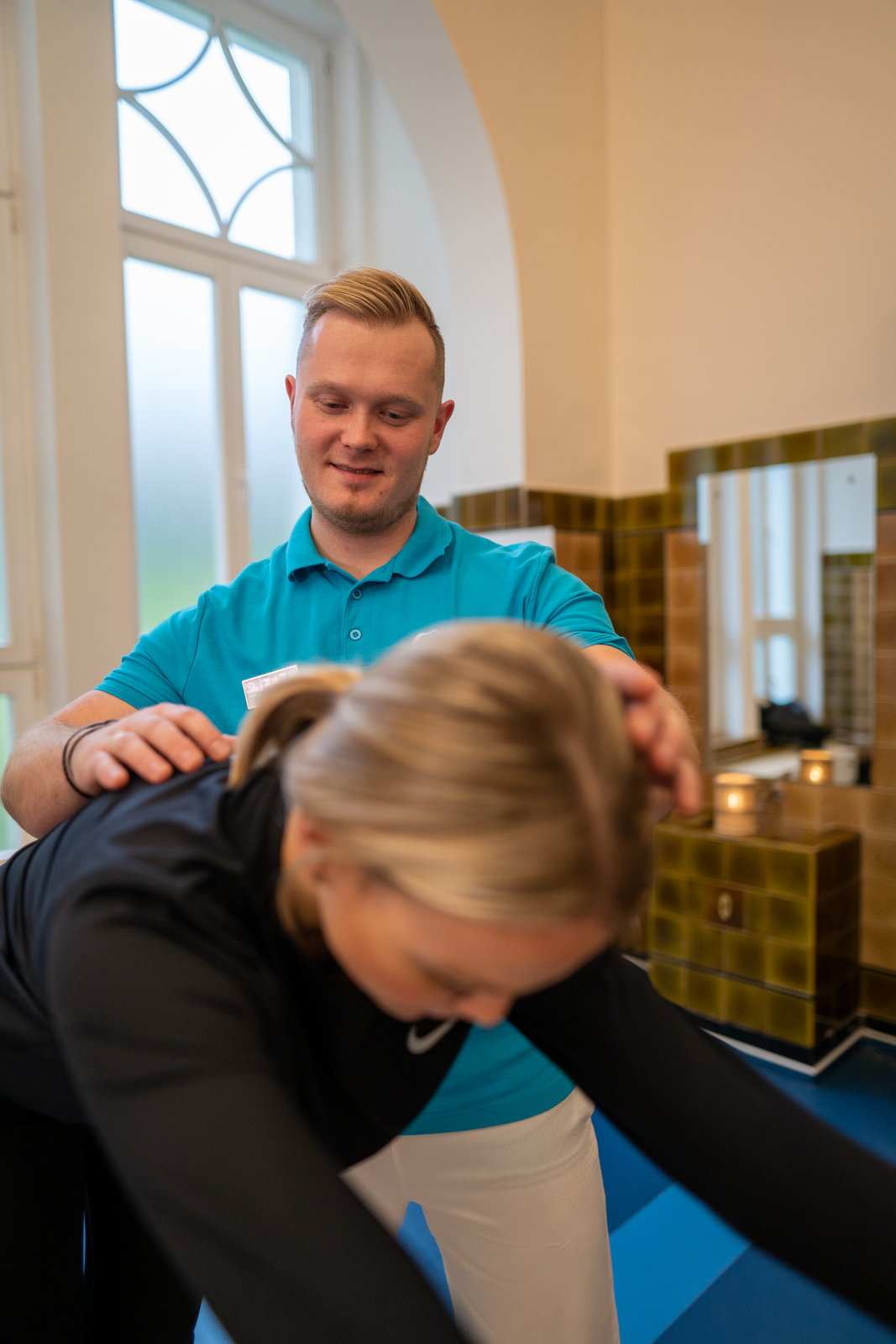 Hlavní fyzioterapeut společnosti Léčebné lázně Mariánské Lázně – Ensana učí fyzioterapeutické cviky: vede hostku při bočním protažení.