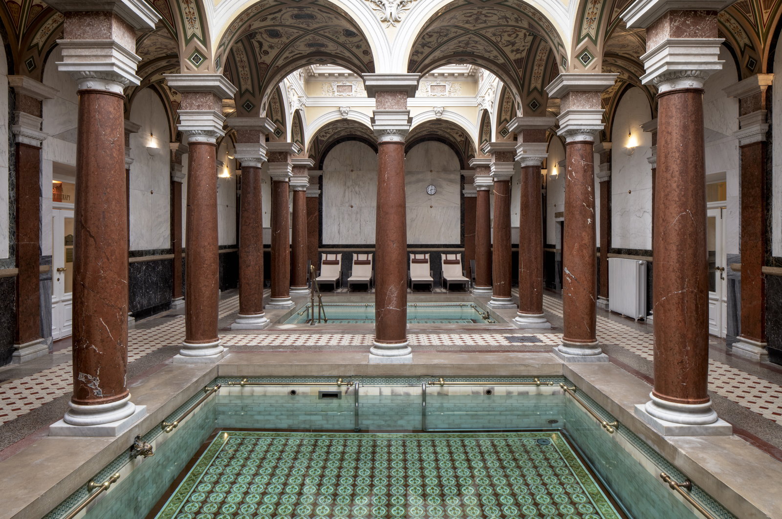 Neo-Renaissance bath hall with red marble columns, vaulted ceiling and two mosaic-tiled pools