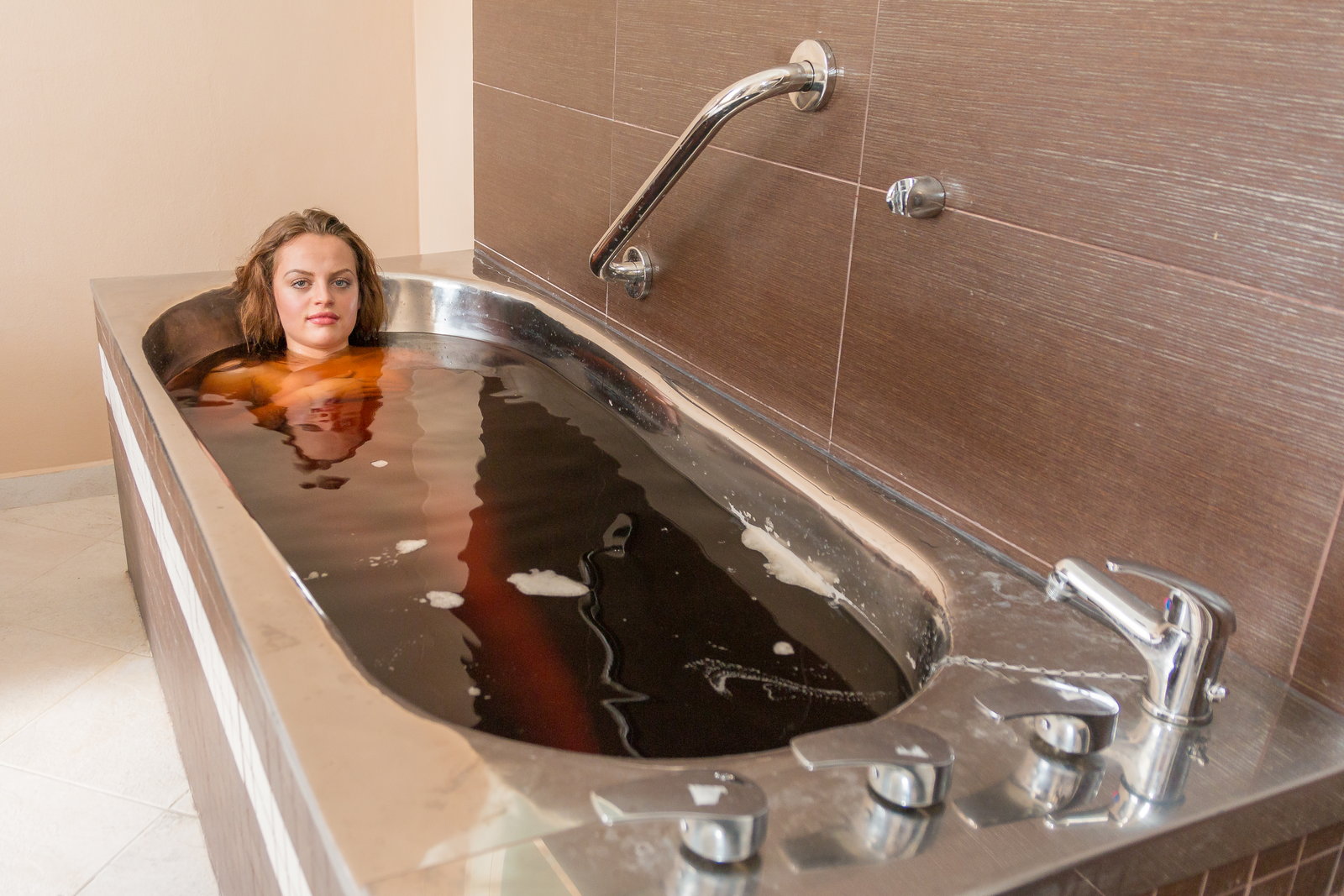 A woman rests with a calm expression in a dark mineral water bath, the water reaching her shoulders