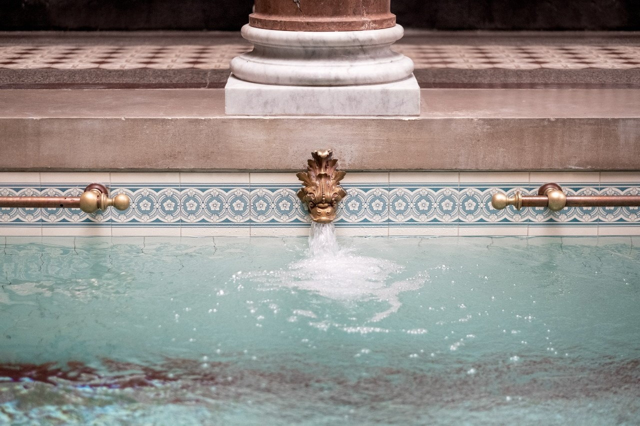 Ornate bronze fountain head pouring water into a turquoise spa pool