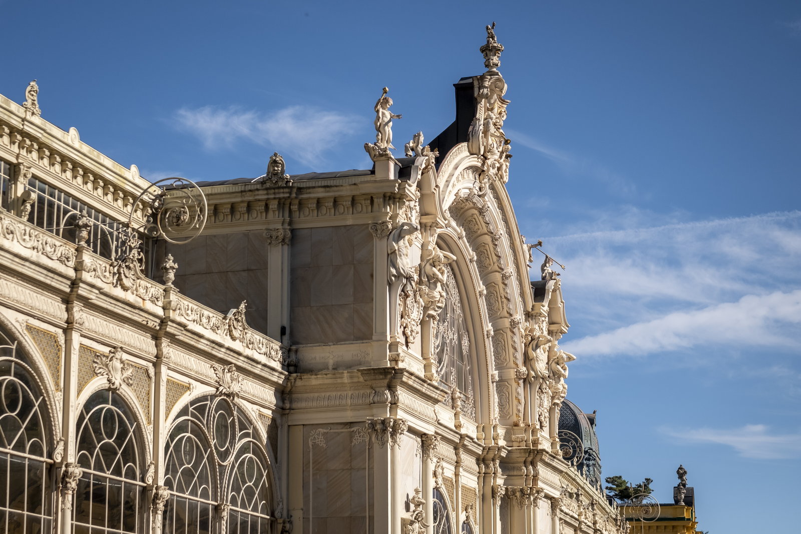 Corner detail of an ornate spa building with rooftop statues and iron balconies