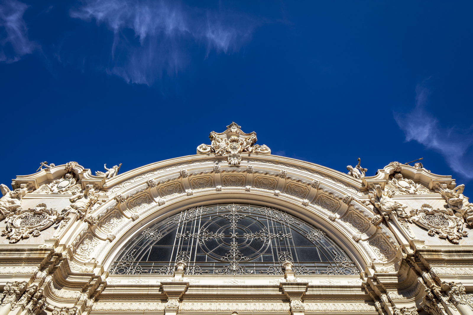 Ornate cream rococo gable with stucco figures and an arched wrought-iron window
