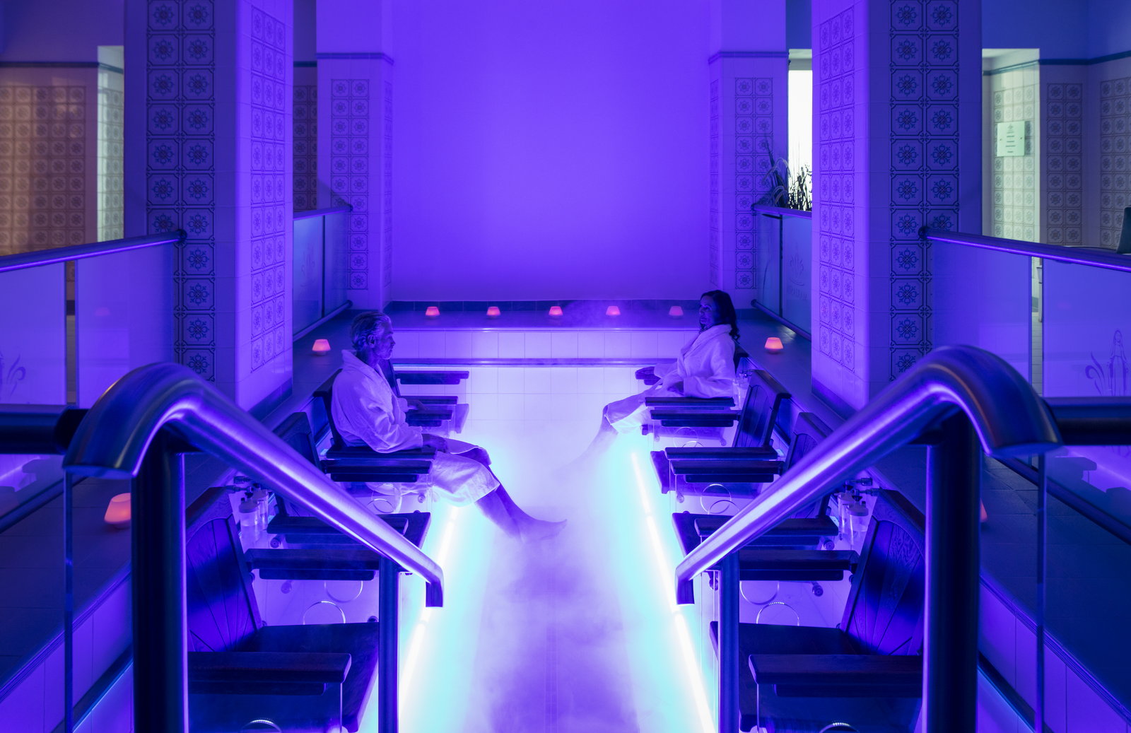 Gäste in Bademänteln ruhen neben dem CO₂-Becken im violetten Licht.