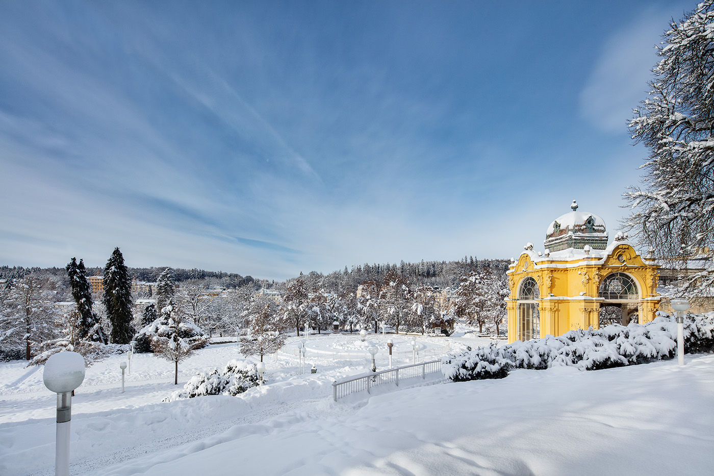 The snow-covered spa park with the colonnade and conifers
